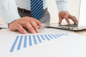 棒グラフの印刷されたレポートに手を載せパソコンをいじるネクタイをつけた男性