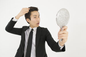驚いた表情で鏡を見ながら頭髪を触る男性